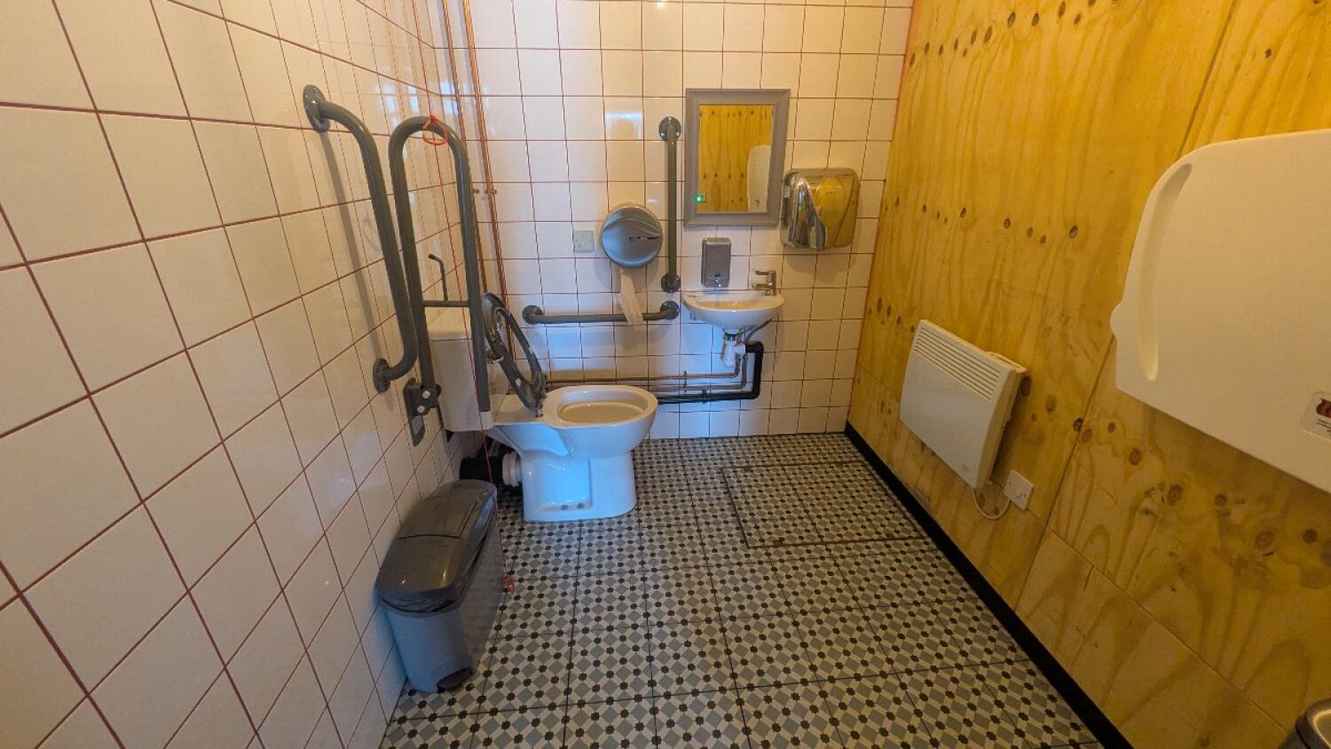 From door facing straight. Baby change table on right. Sink on back. Toilet on back left. Emergency pull cord to its left.