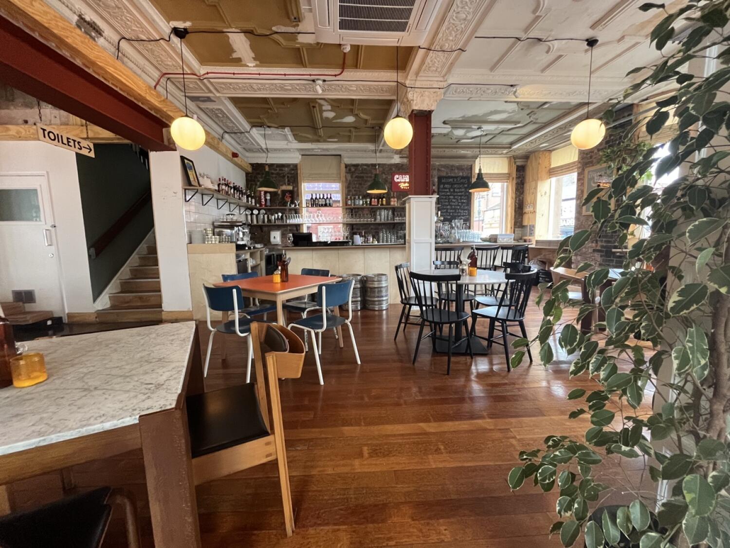 From archway facing right. Bar counter at back. Tables and chairs spread ahead.