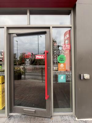 Glass door with a grey frame and red handle on right. Pull to open.