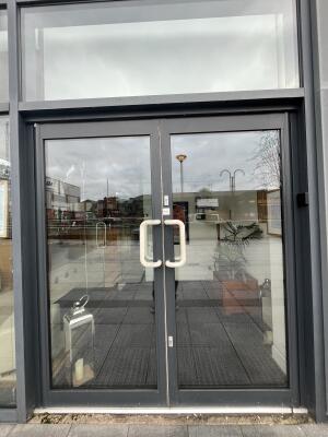 Glass double door with grey frame and metal handles in centre. Pull to open.