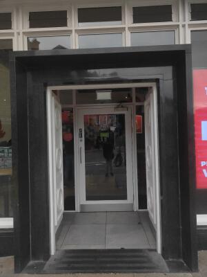 From street facing venue. Black archway leading to white framed glass door.