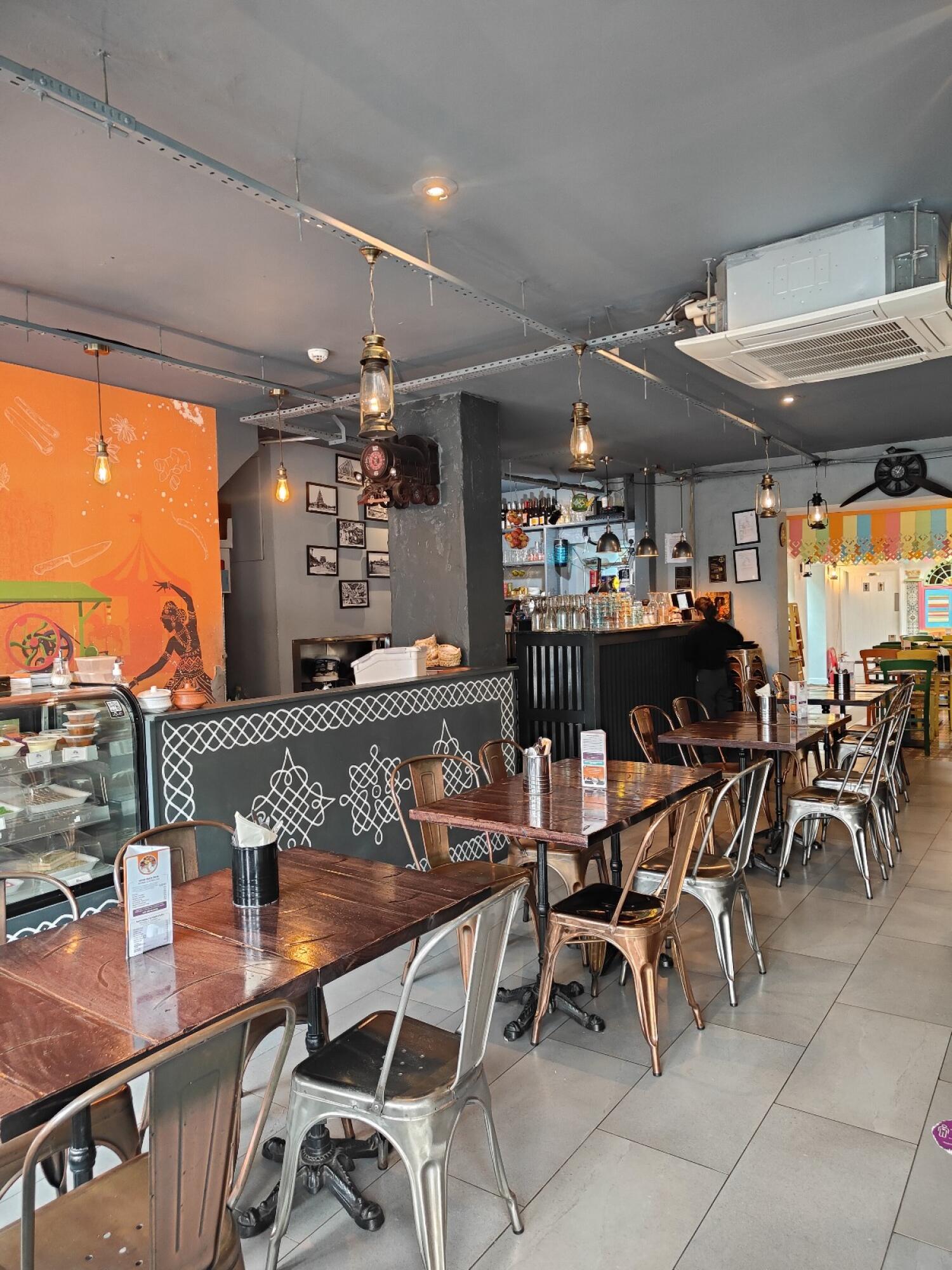From welcome desk facing left. Tables and chairs ahead. Food display counter along back wall.