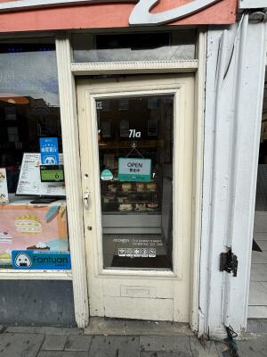 From sidewalk facing venue. Off white framed glass door ahead. Push door handle on left to open inwards.