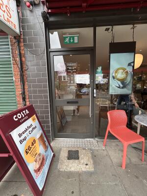 Glass door with grey metal frames ahead. Push metal bar on right to open. Call for assistance button to its right.