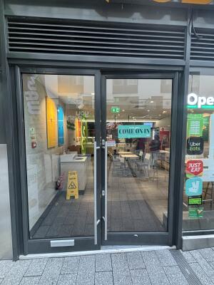 From mall sidewalk facing venue. Black framed glass doors ahead. Push silver handles in centre to open.