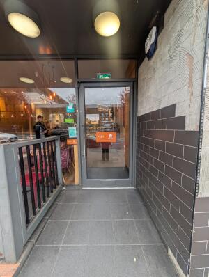 Archway in front. Fencing on left. Grey frame glass doors at back. Silver metal handle on left. Push to open.