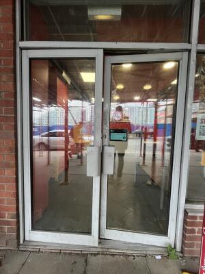 Glass double door with a grey frame and metal handle in centre. Push to open.