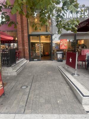 From side walk facing venue. Built-in ramp going up to entrance at back. Outdoor seating on the right.
