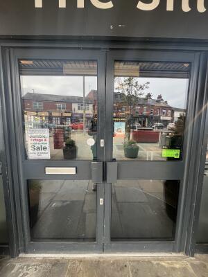 Glass double door with grey frame and metal handles in centre. Push to open.