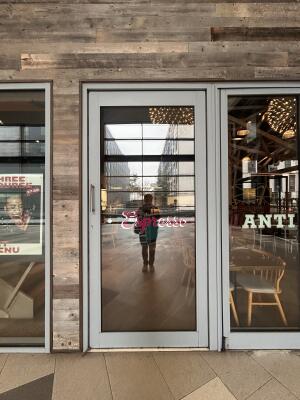 From path facing venue. Glass door with grey metal frames ahead. Pull from left to open.