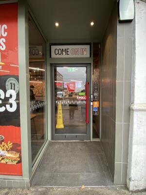 Opening to the entrance door. Grey framed glass door. Pull red long metal handle from right to open.