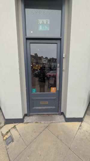 Glass door with grey frame. Push handle on left to open.