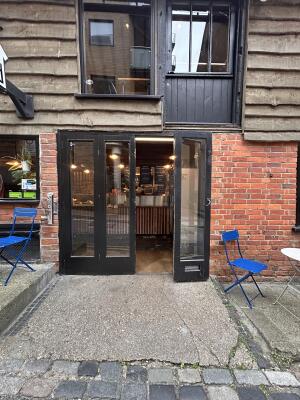 From side walk facing venue. Glass door with black metal frame ahead. Pull from center to open.