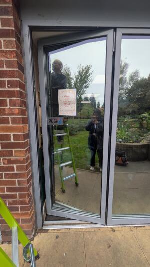 Glass door with metal frame. Push handle on left to open.