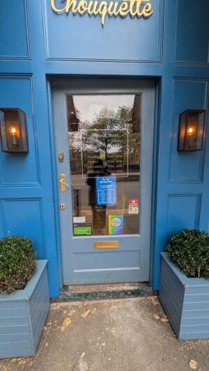 Glass door with blue wooden frame. Push handle on left to open.