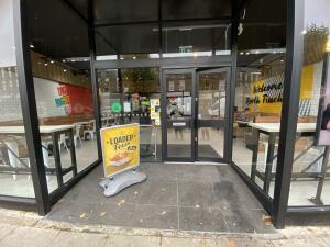 From street facing venue. Opening ahead. Door at back right. Framed sign to the left of entrance door.