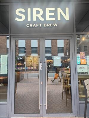From sidewalk facing venue. Grey framed double glass doors. Push silver handle in centre to open.