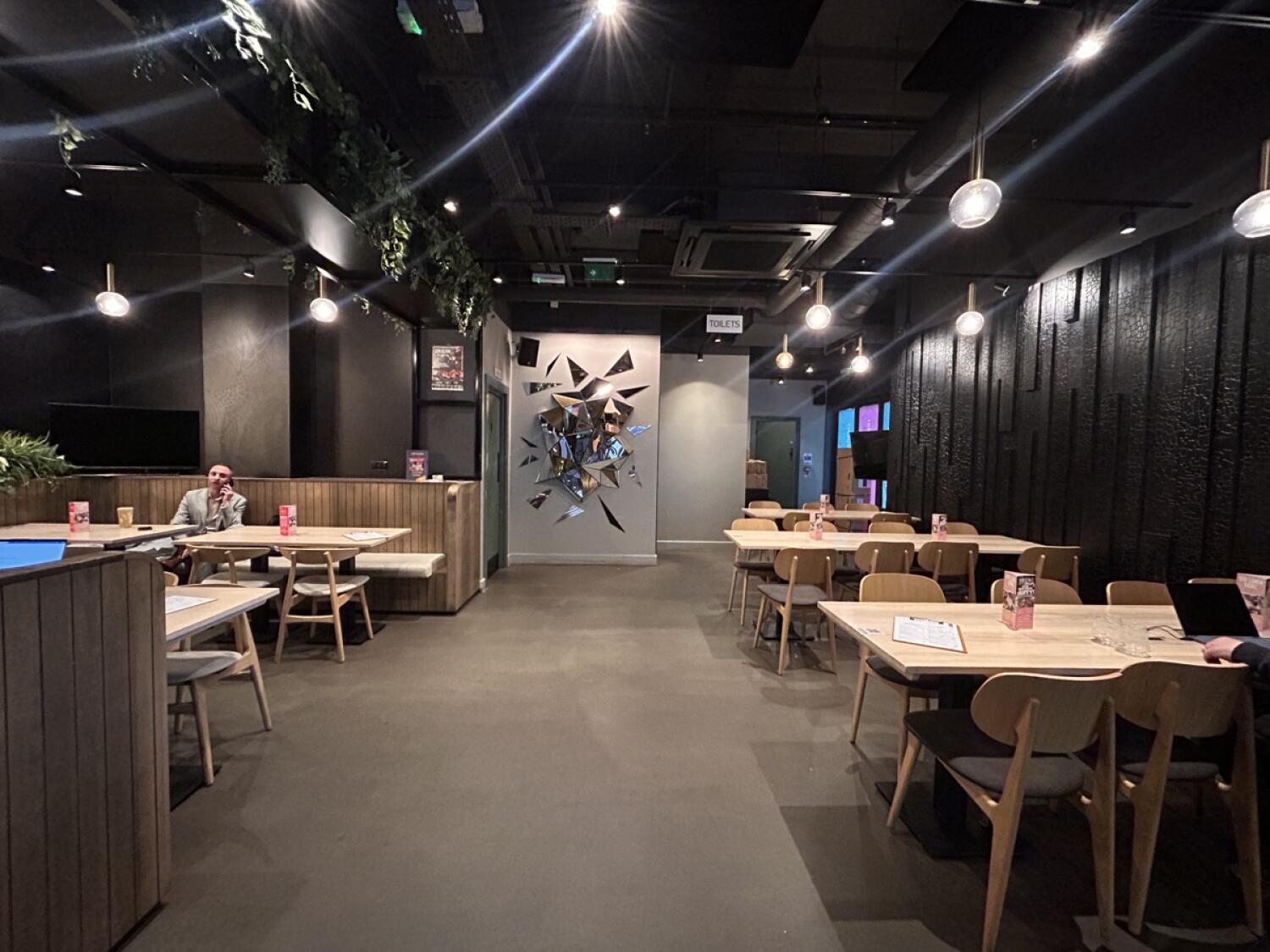 From after bathroom facing straight. Half-booth on left. Non-accessible bathroom behind. Chairs and tables on right.