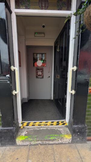 Black, wooden door with white frame ahead. Push from left to open. Grabrails on both sides of doorframe.