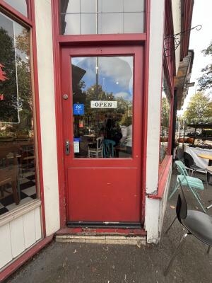 Glass door with red wooden frame and metal handle on left. Push to open.