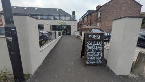 From street facing venue. Pillars on both sides. Information board on right. Path to doors in center.
