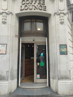 From sidewalk facing venue. Brown framed archway leading to white framed doors right after. Push white bar in centre to open.
