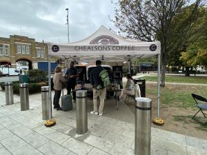 From sidewalk facing the venue. Metal pillars ahead. Opening of the coffee stall behind.