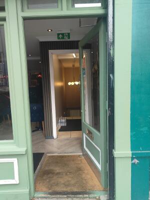 From sidewalk facing venue. Green door with half glass panel ahead. Push silver handle at top left to open.
