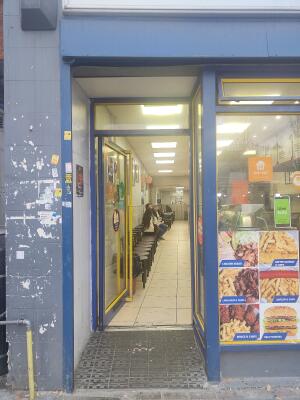 From sidewalk facing venue. Blue framed glass door ahead. Push yellow handle on right to open.