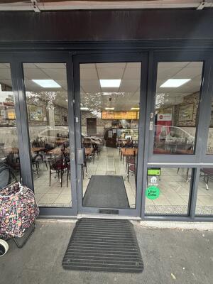 From street facing venue. Grey framed glass door ahead. Push door from left to open inwards. Ramp before foot of door.