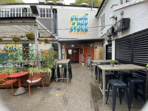From alley facing straight. Table and chairs on left. High tables and stools on left and right sides. Entrance door at back.