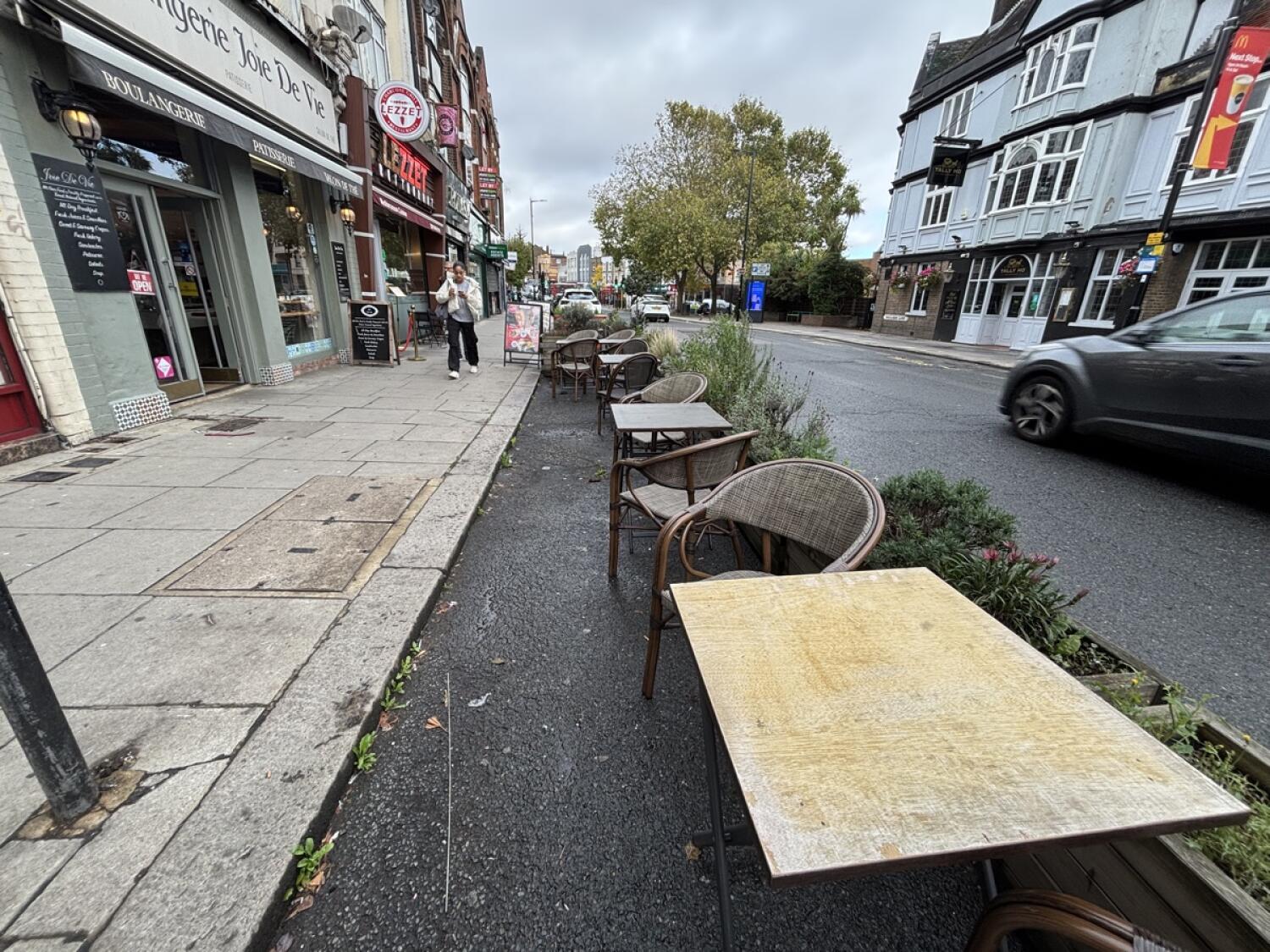 From bottom of ramp facing left. Tables and chairs along right. Planters to their right. Step up along left.