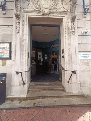 From street, facing venue. Steps at back. Black handrail on both sides. Grey wooden doors at top, push from middle to open.
