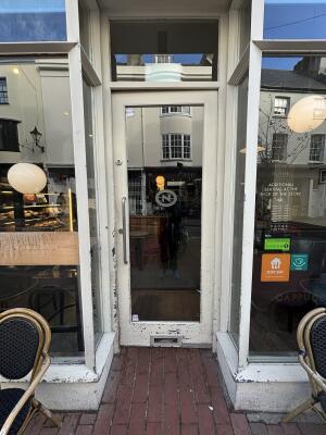 From street facing venue. White framed glass door ahead. Push silver handle on left to open door inwards.