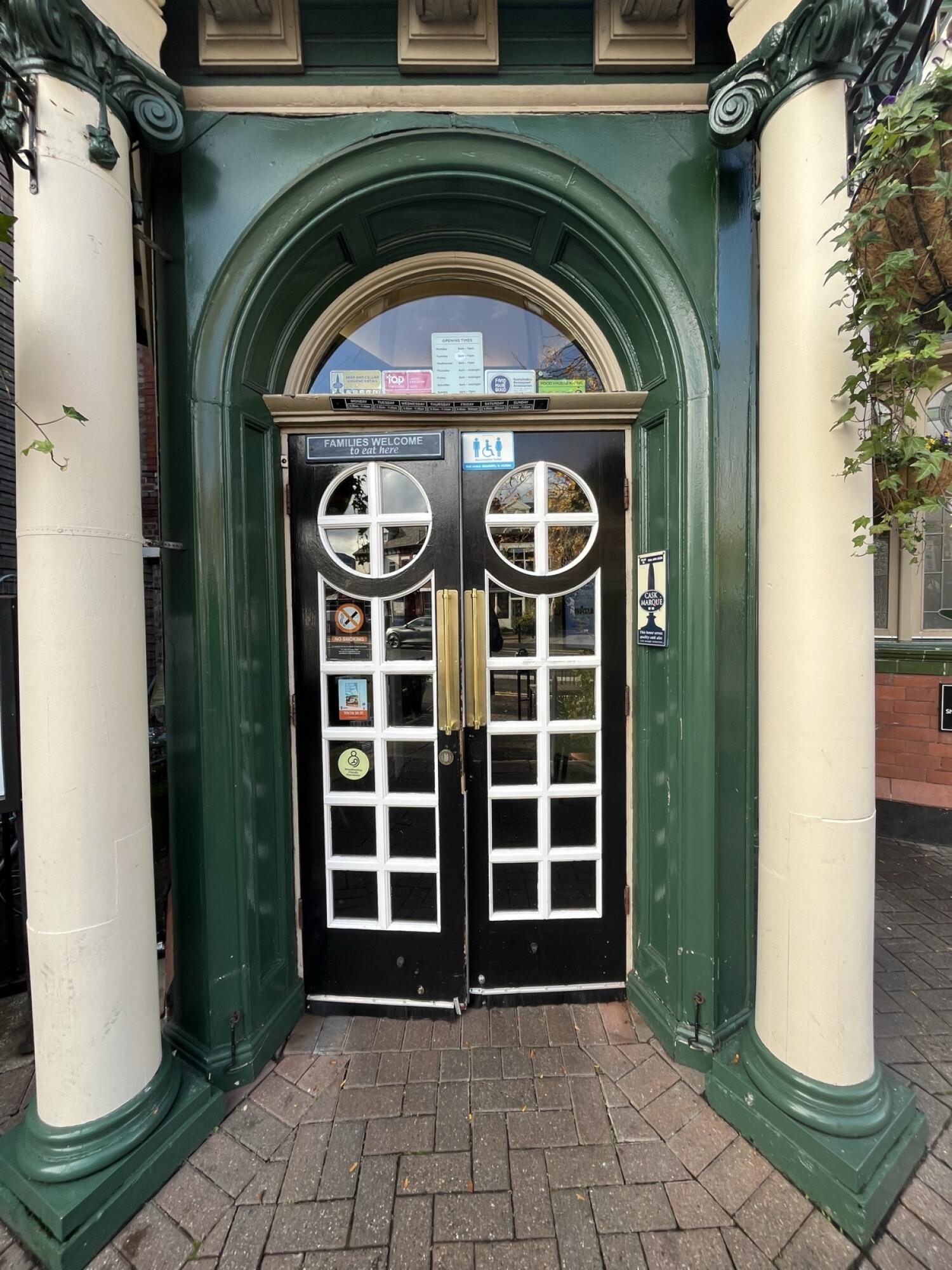 From end of open space facing straight. Glass double door with green frame and handles in centre. Push to open.
