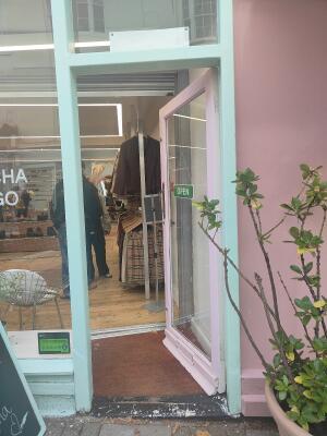 From sidewalk facing venue. Pink framed glass door ahead. Push bronze handle on left to open.