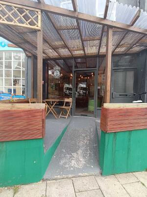 From street facing venue. Opening ahead. Woden wall dividers on either side of opening. Slope up ramp to door following.