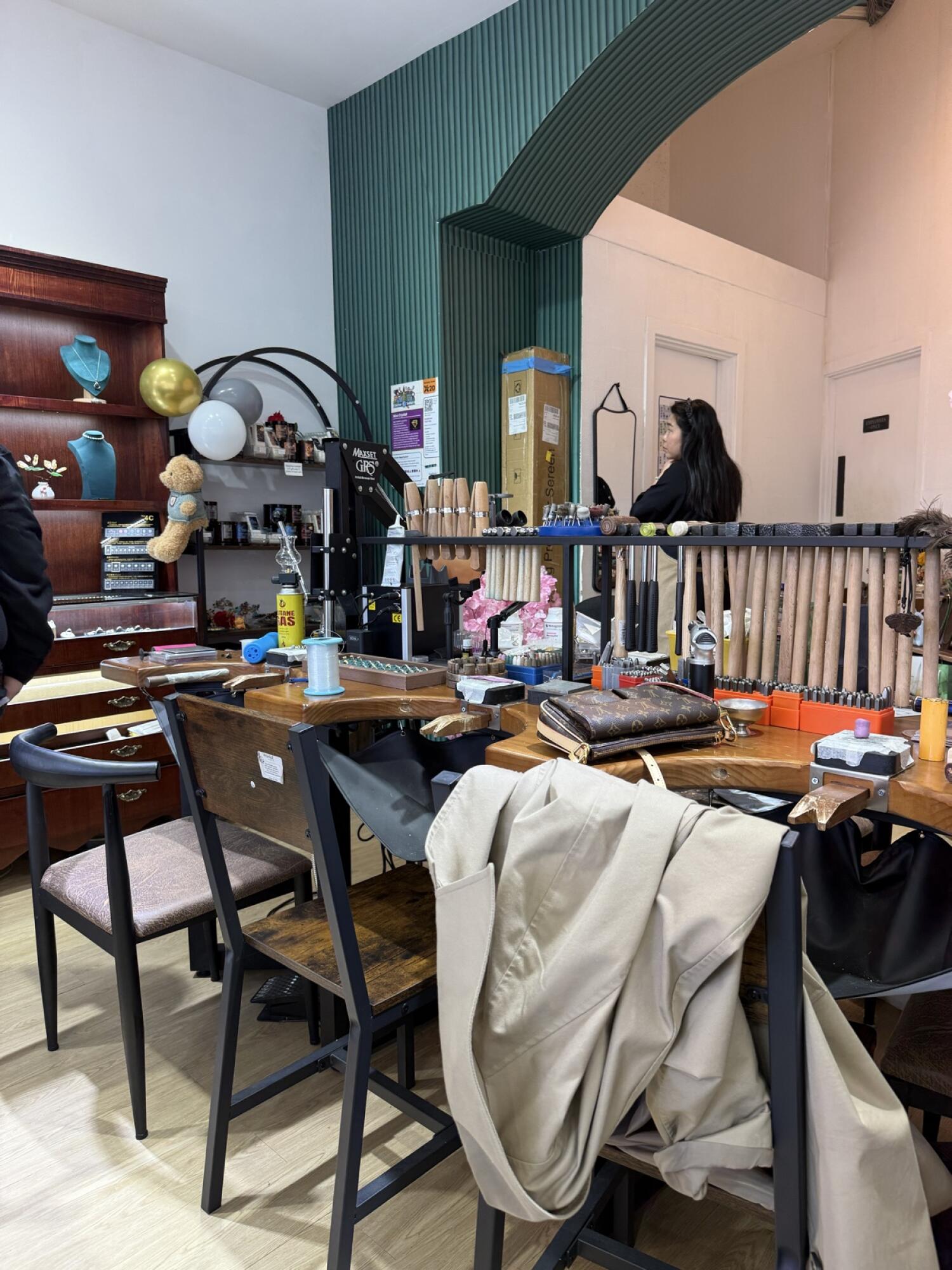 From center of workshop facing straight. Workbenches with tools in front. Shelving with display busts left. Doorways visible at back right.
