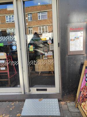 From sidewalk facing venue. Grey framed glass door ahead. Push silver handle on left to open.