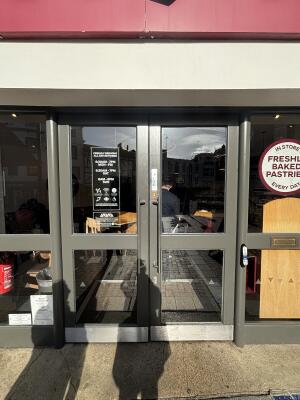 From street facing entrance. Grey framed glass doors ahead. Push silver handles in centre to open inwards.