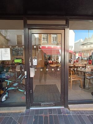 Glass door with black, metal frame. Push from handle on left to open.