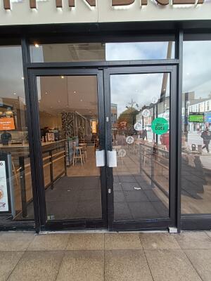 From street facing venue. Black framed glass doors ahead. Pull doors from centre to open outwards.