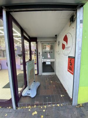 From sidewalk facing the opening. Framed sign on left. Entrance door behind.
