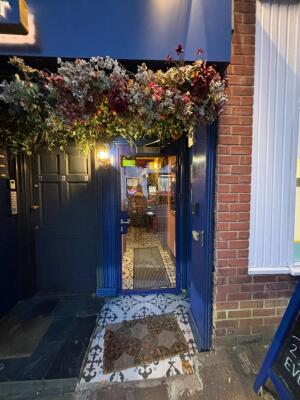 From sidewalk facing venue. Blue framed preceding glass door ahead. Pull grey handle on left to open.