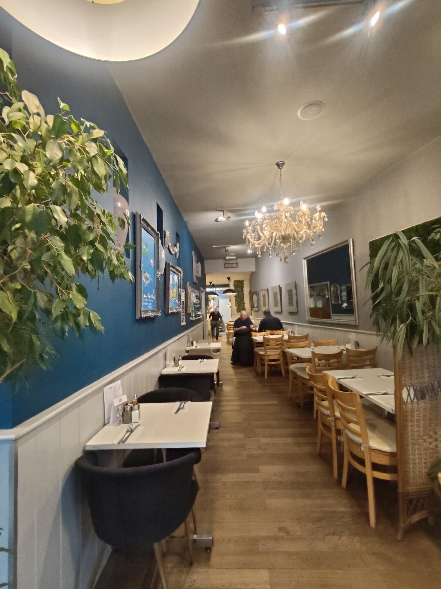 From entrance facing straight. Tables and chairs on both sides. Open kitchen counter at back left.