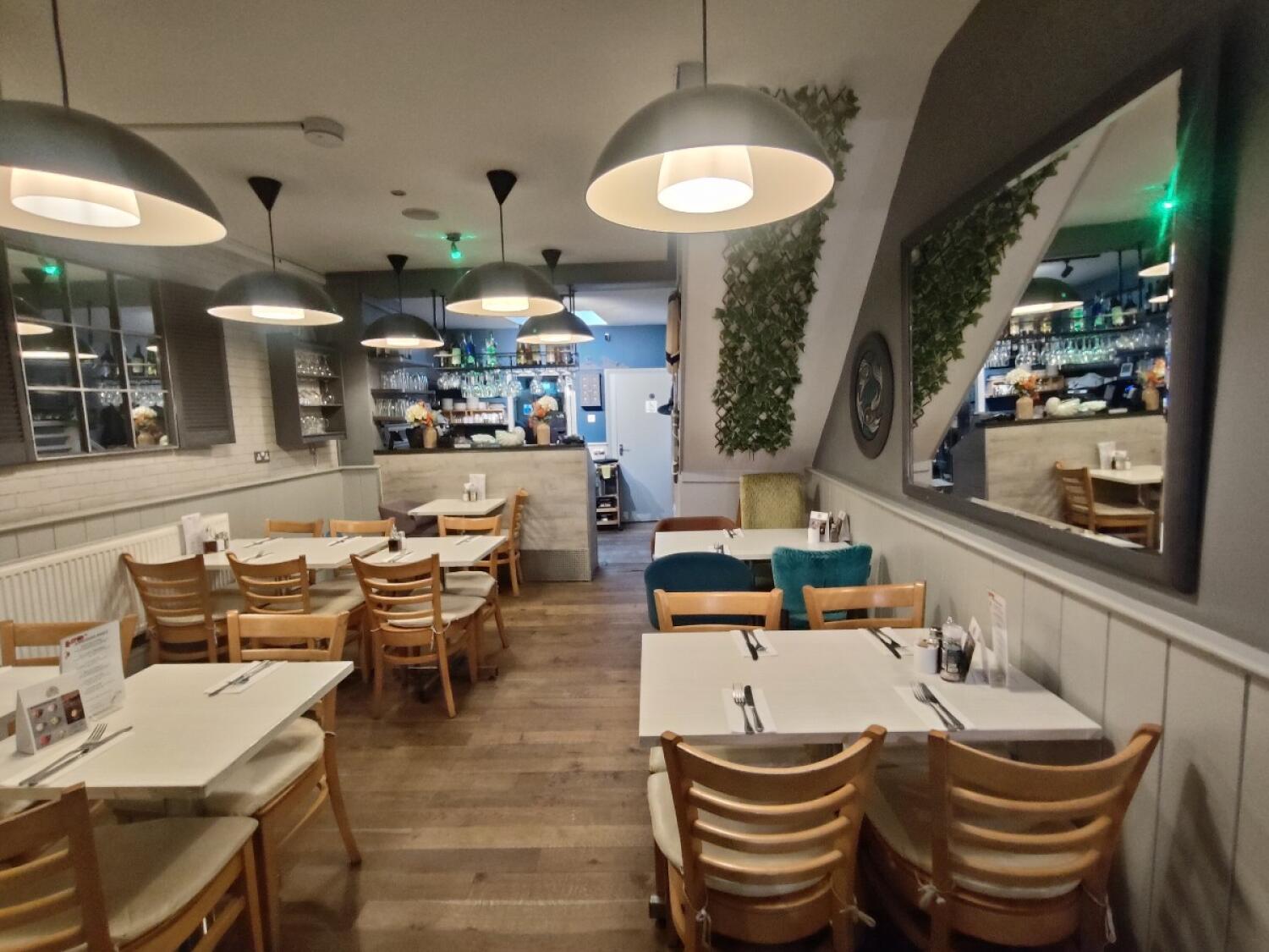 From open kitchen counter facing straight. Tables and chairs on both sides. Staff counter at back left.