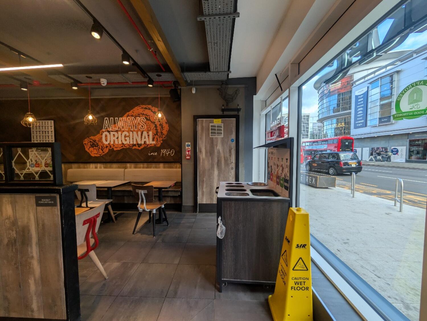 From entrance facing right. Bin on front right. Tables, chairs, and half booths on back left. Wooden barrier on front left.