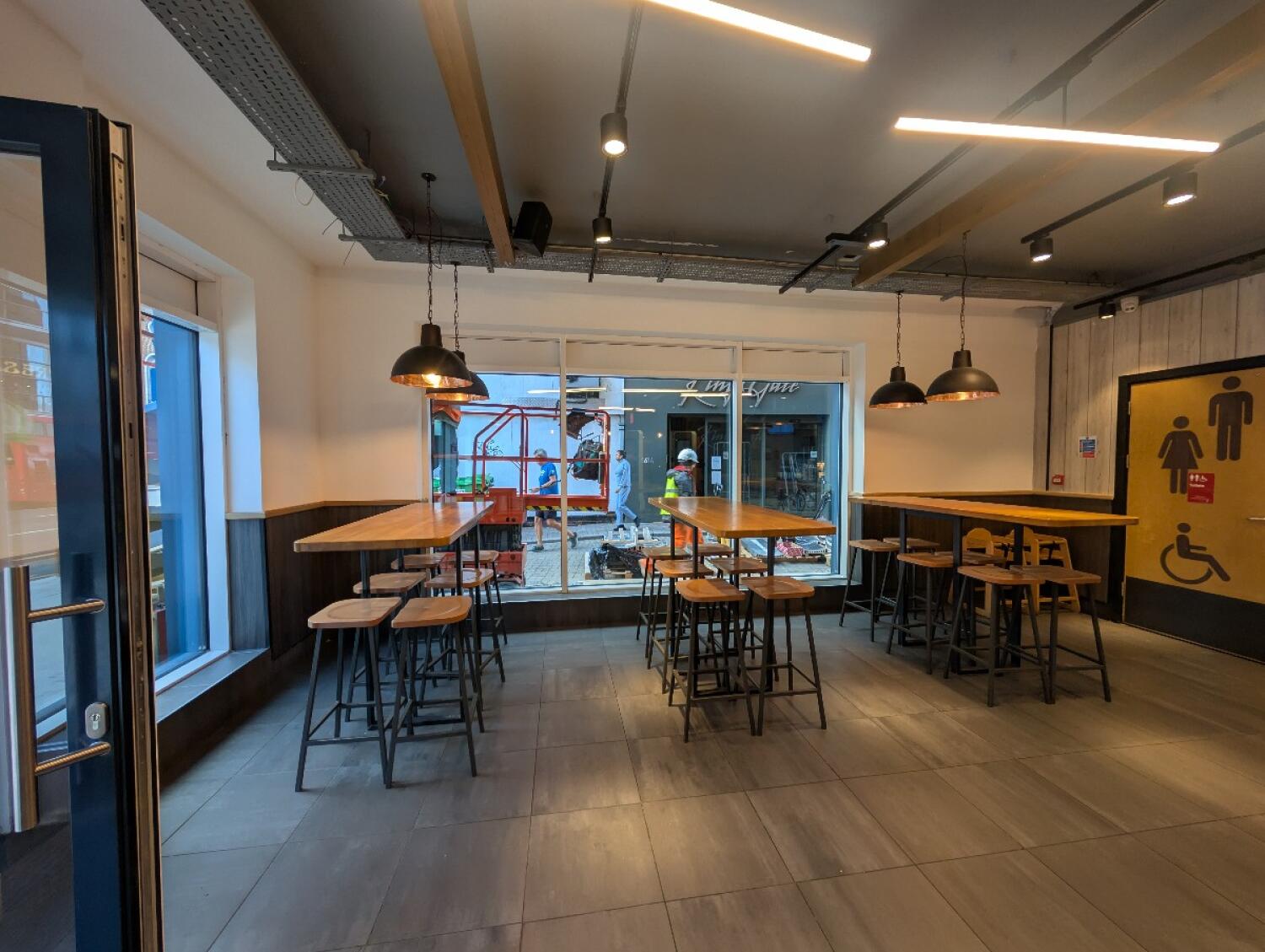 From entrance facing left. High tables and stools along back. Bathroom door at back right.