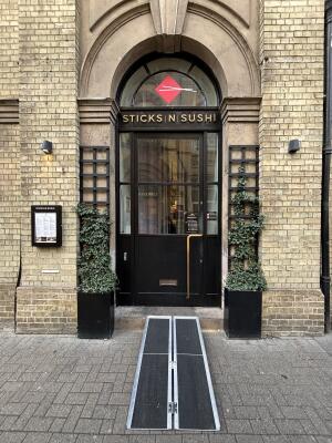 From street, facing venue. Archway with step at back, planters on both sides. Black framed glass door behind. Pull from handle on right to open.