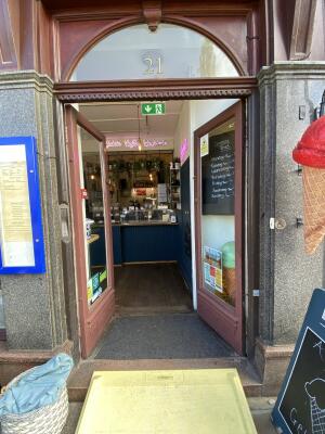 Dark red framed glass door. Push from centre to open. Assistance bell on right side of door.